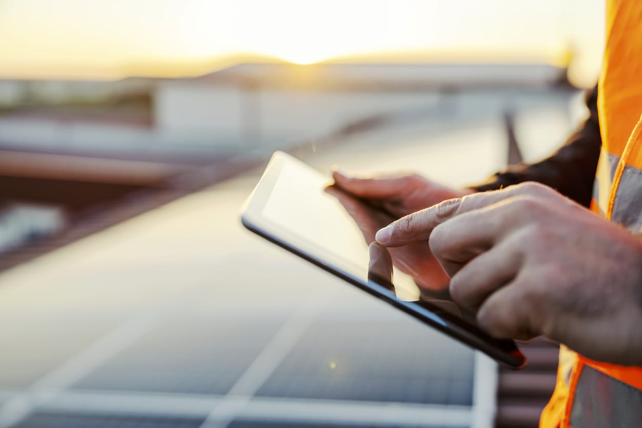 Technician overseeing commercial solar panel installation using a tablet at a solar energy site